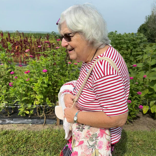 A Newton Village tenant smiles while walking through a vibrant flower garden at the Iowa Flower Farm, enjoying the fresh air and colorful blooms.