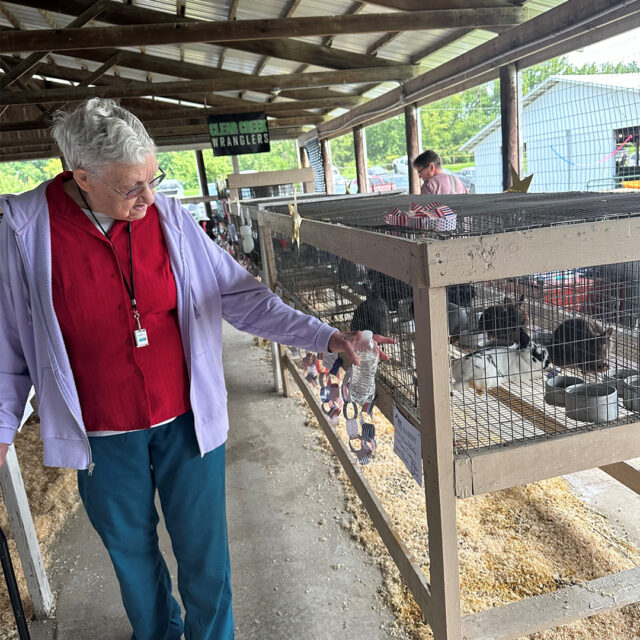 A Newton Village tenant enjoys visiting the animal barns at the Jasper County Fair, gently interacting with rabbits in cages, surrounded by a rustic fair setting.