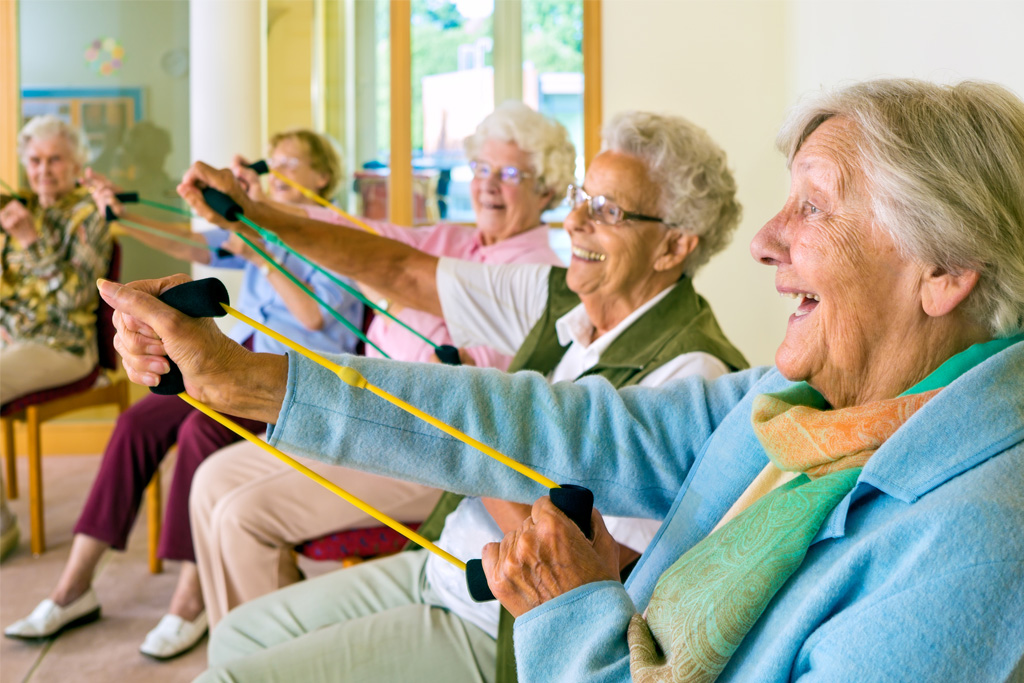 Older adults participating in a seated resistance band exercise class, smiling and engaging in movement for Therapy Month.