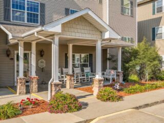 Front entrance of Newton Village Assisted Living with rocking chairs, landscaped flowers, and welcoming porch.