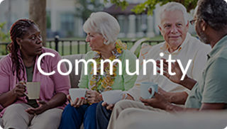 Group of older adults sitting together outdoors holding coffee mugs and talking, with the word “Community” displayed, representing connection and social living like at Newton Village