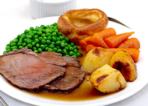 Plated meal with sliced roast meat, peas, carrots, roasted potatoes, and gravy, representing dining options like at Newton Village