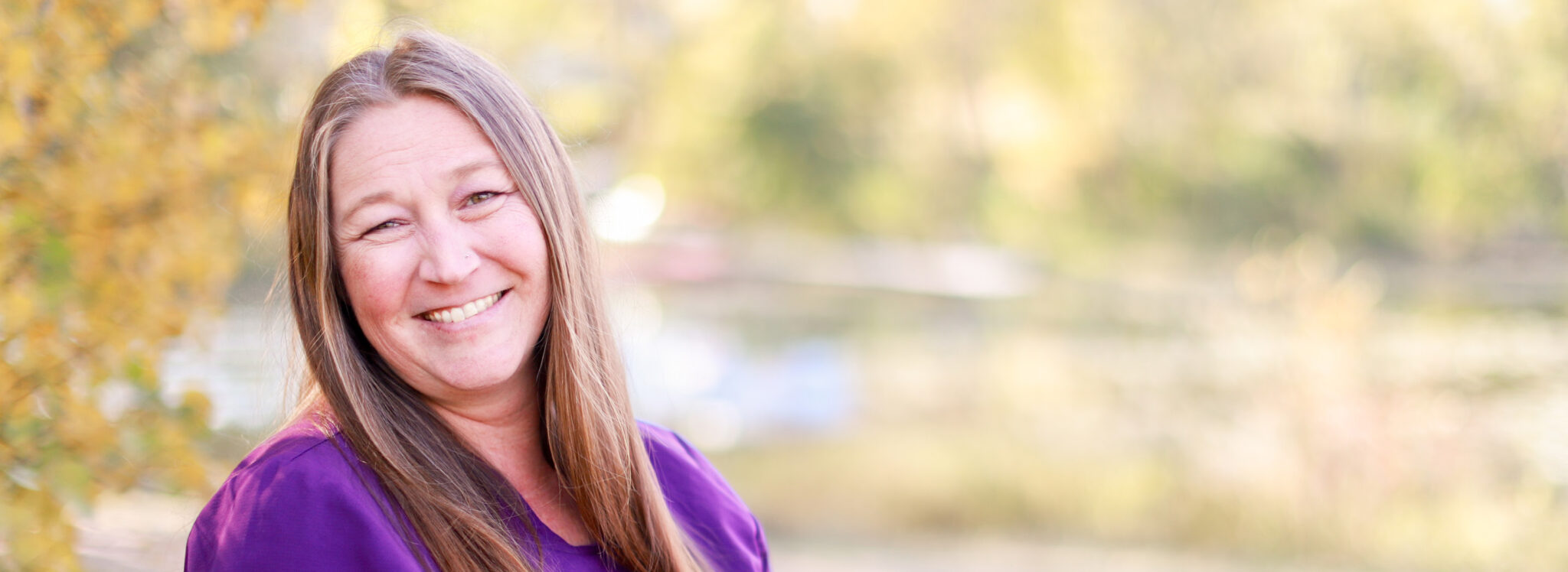 Employee portrait outdoors near a natural setting with trees and water, representing staff like at Newton Village