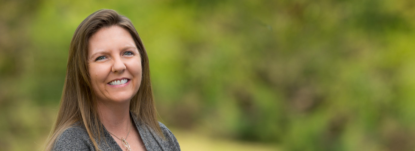 Employee portrait outdoors with a natural green background, representing staff like at Newton Village