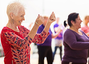 Group of older adults participating in a fitness class with arm movements in a bright activity space, representing programs like at Newton Village