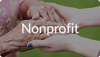 Close-up of two hands gently holding an older adult’s hands with the word “Nonprofit” displayed, representing compassionate care and support through nonprofit services like at Newton Village