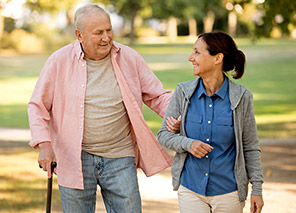 Two older adults walking arm in arm along a tree-lined outdoor path in a park setting, representing outdoor activities like at Newton Village