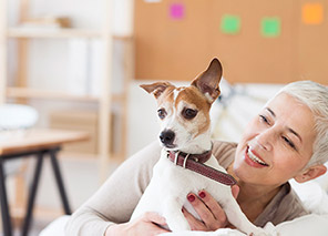 Adult holding a small dog while seated indoors in a bright room, representing pet-friendly living and companionship like at Newton Village