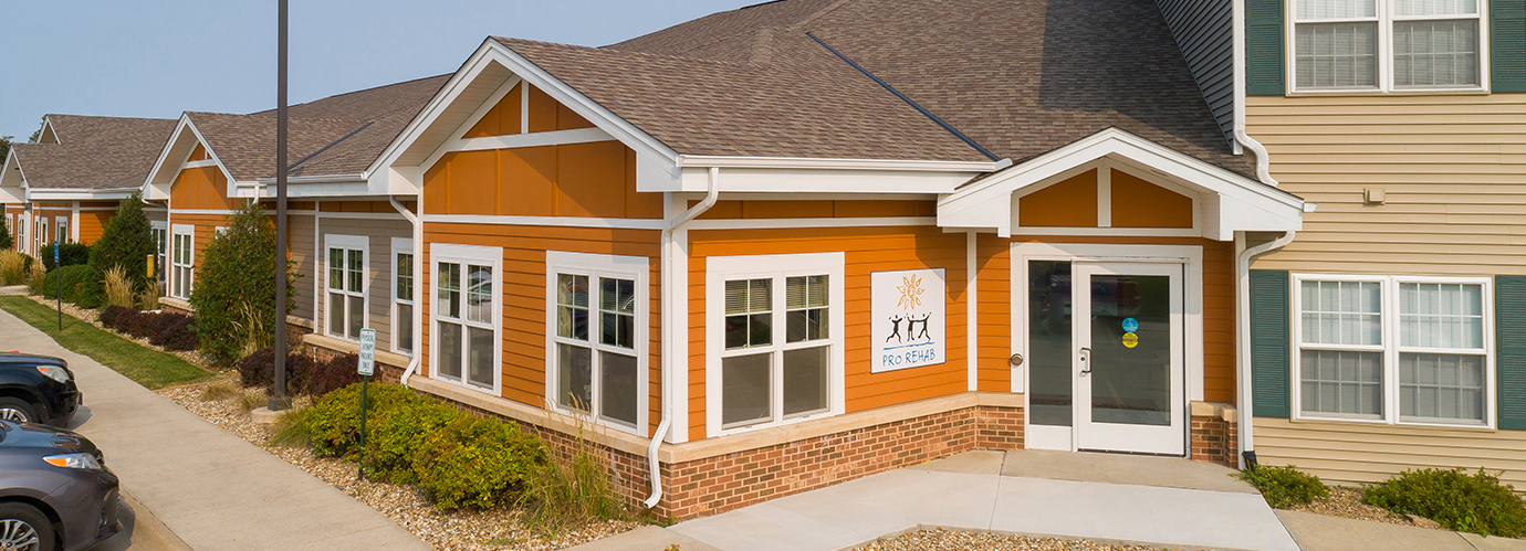 Exterior of the Pro Rehab building with orange siding, white trim, entrance door, and signage at Newton Village